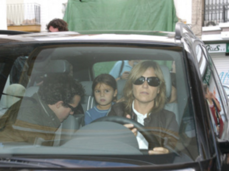 Una familia en el asiento trasero de un coche, con una persona al volante, en un entorno urbano.