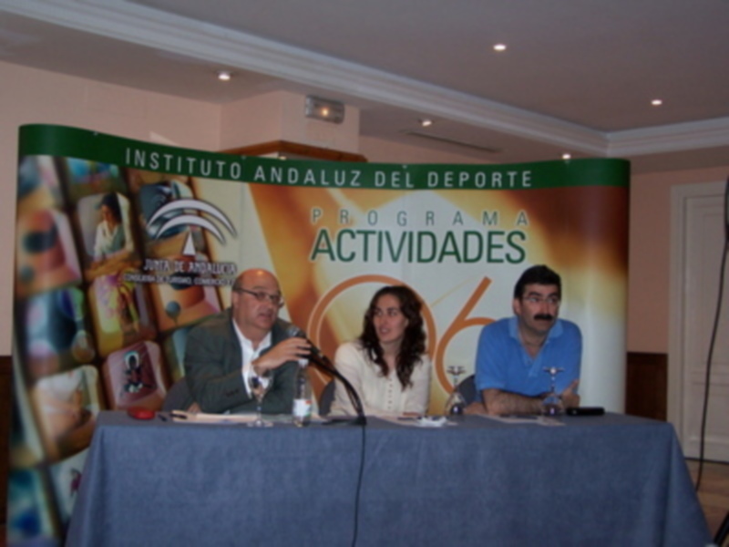 Tres personas sentadas en una mesa con un cartel de la Fundación Andaluza del Deporte en el fondo.