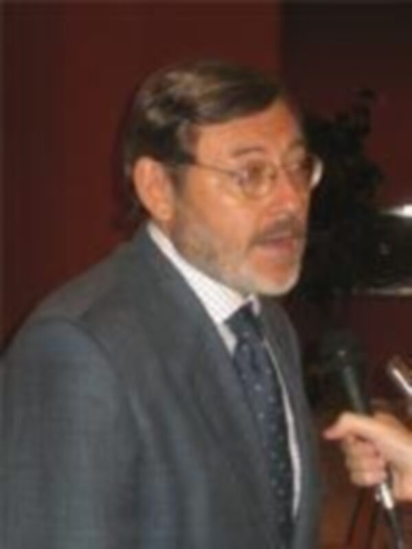 Hombre en traje hablando en un evento público, sosteniendo un micrófono.