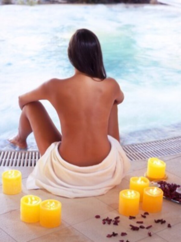 Una mujer se relaja en una piscina con velas y flores alrededor.