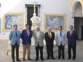 Grupo de hombres en trajes formales posando frente a una estatua y azulejos decorativos.