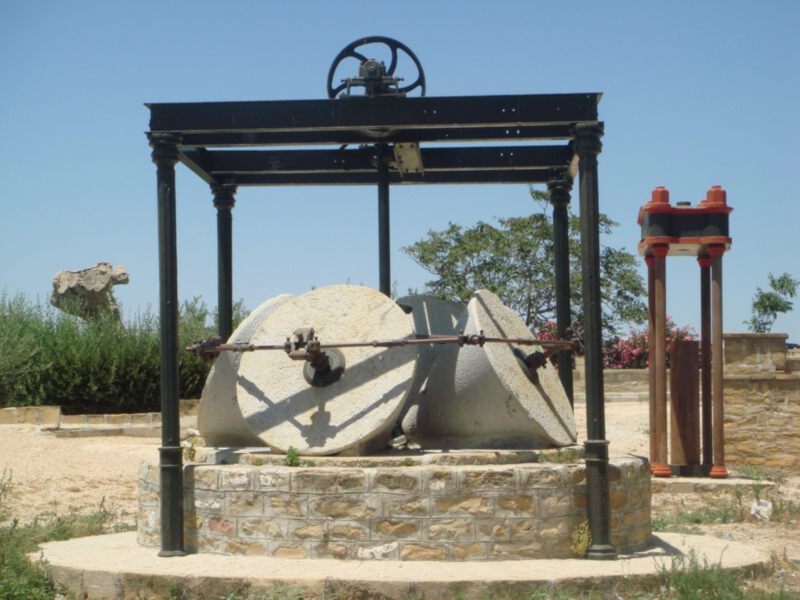 Un antiguo molino de piedra en un parque, con una estructura metálica y una base de piedra.