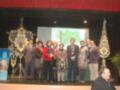 Grupo de personas en un escenario, posando para una foto. En el fondo, hay un proyector y banderas con símbolos heráldicos. La imagen parece ser de una ceremonia o evento formal, posiblemente un congreso o conferencia.