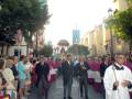 Procesión religiosa con sacerdotes y fieles en una calle urbana.