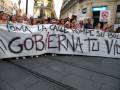 Manifestación en una calle, con personas sosteniendo un cartel que dice '¡Gobiérrnato tu vida!' y otros carteles en el fondo.