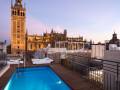 Un hermoso balcón con una piscina azul brillante y sillas de relajación, frente a la icónica Giralda en Sevilla.