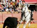 Jinete en acción durante una corrida de toros en arena, rodeado por un público atento.
