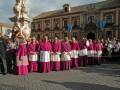 Un grupo de sacerdotes en túnicas moradas posa en la plaza frente a un edificio histórico con banderas de España y Venezuela.