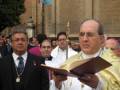 Un sacerdote sostiene un libro abierto durante una procesión religiosa en una plaza histórica.