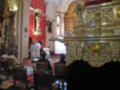 Interior de una iglesia con altares ornamentados y personas asistiendo a una ceremonia religiosa.