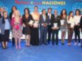 Una foto de un grupo de personas posando juntos en una alfombra roja. Algunos están sosteniendo premios y otros sonríen para la cámara. La imagen está en un escenario con una bandera de fondo y el texto "Festival de las Naciones".