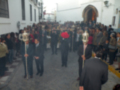 Una procesión religiosa en una calle con gente vestida formalmente, algunos portando objetos ceremoniales.
