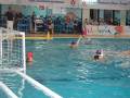 Equipo de waterpolo en acción en una piscina con un marcador de tiempo y publicidad en el fondo.