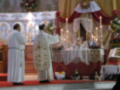 Imagen de una iglesia con dos sacerdotes en el altar, rodeados por flores y velas.