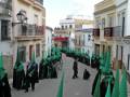 Desfile procesional en una calle de la ciudad, con participantes vestidos de negro y portando banderas verdes.