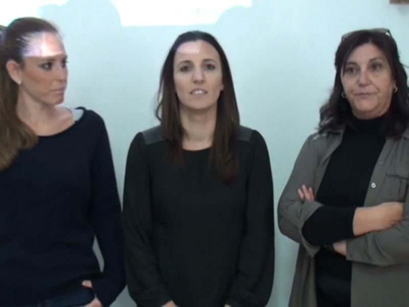 Tres mujeres de pie frente a una pared blanca, una con el cabello largo y los otros dos con el cabello corto.
