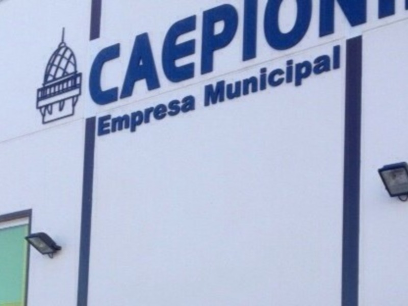 La fachada de un edificio blanco con el logotipo y nombre "CAEPION" en letras azules, junto con la frase "Empresa Municipal". La estructura tiene dos ventanas laterales y una lámpara de techo en la parte superior izquierda.