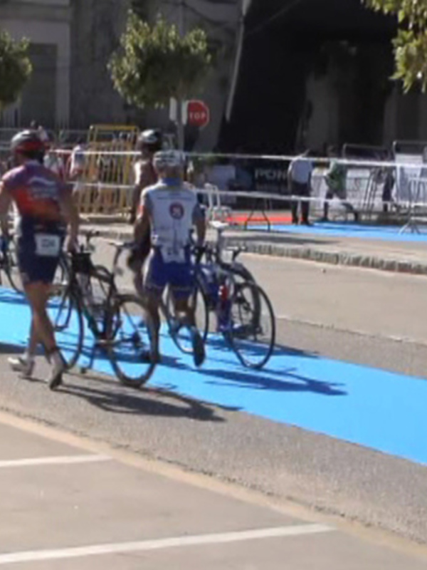 Desfile de ciclistas y corredores en una carretera con carriles separados por un área azul.