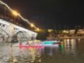 Noche de remo bajo el Puente de Triana, Sevilla, con luces y espectadores en el puente.