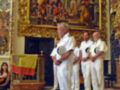 Un grupo de marineros en uniforme blanco se encuentra frente a un gran cuadro dorado en una iglesia. La imagen muestra una bandera española colgada a un lado y el suelo es de baldosas negras y blancas.
