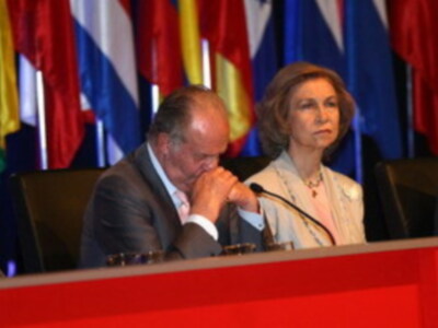 Dos personas sentadas en un escenario con banderas de diferentes países al fondo.