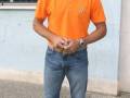 Un hombre con camisa naranja, jeans y zapatillas azules.