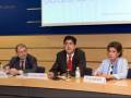 Tres personas sentadas en una mesa, con un fondo de una pantalla que dice "Derecho de". La imagen parece ser de una conferencia o reunión formal.