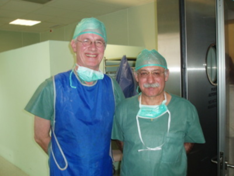 Dos médicos sonrientes en un hospital, uno con uniforme azul y el otro con verde.