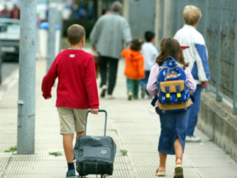Niños caminando en el camino con mochilas y maletas, en un ambiente urbano.