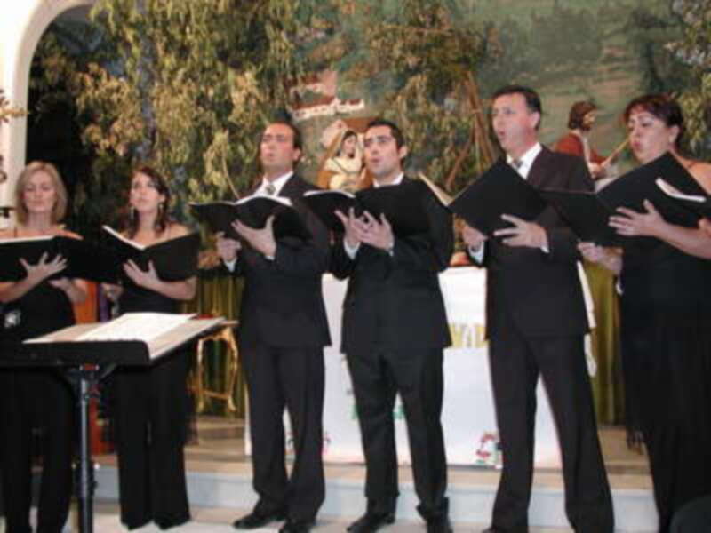 Un grupo de personas cantando en un escenario decorado con una imagen religiosa.