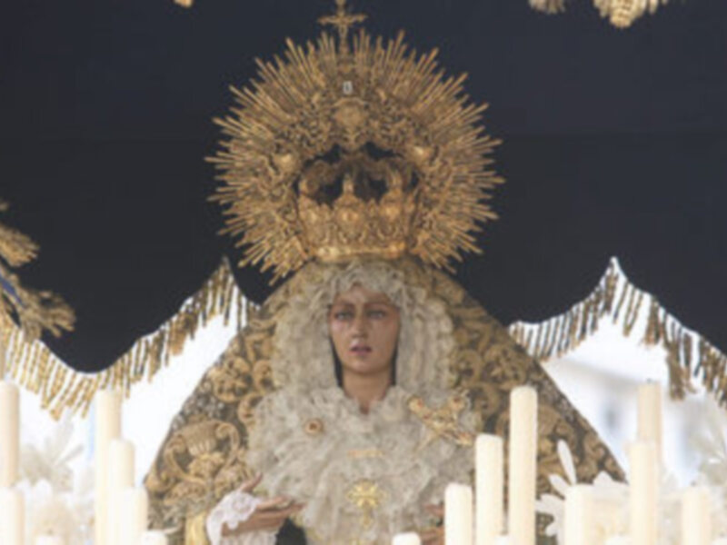 Una figura vestida con trajes tradicionales, posiblemente de un evento religioso o ceremonial. La figura está rodeada por velas y una corona dorada, lo que sugiere un ambiente festivo o ceremonial.