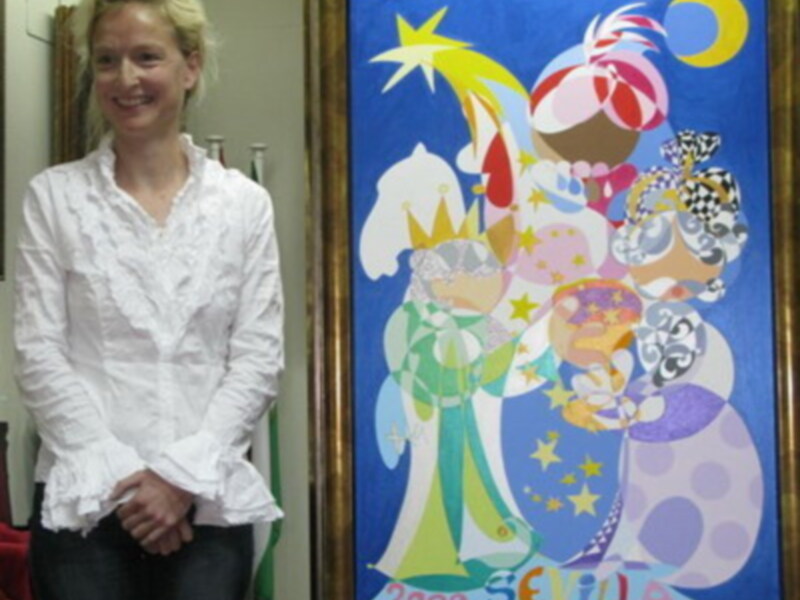 Una mujer sonríe mientras posa junto a un cuadro de arte pop art con figuras coloridas y una estrella. La imagen está firmada "SEVILLA 2005".