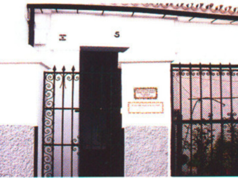 Puerta de metal con rejas y una placa de identificación en la pared de un edificio blanco.