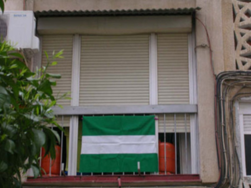 Ventana con persiana y bandera verde y blanca en un balcón urbano.