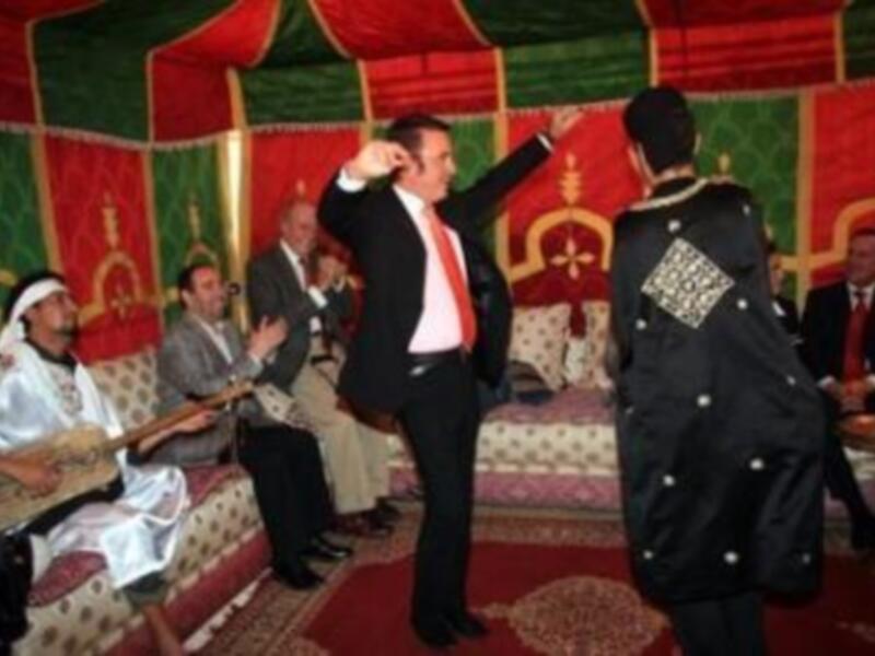 Una escena festiva con personas vestidas tradicionalmente, posiblemente en un evento cultural o religioso. La decoración incluye telas coloridas y adornos que sugieren un ambiente festivo o ceremonial.