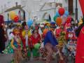 Desfile de carnaval con payasos y globos de colores en una calle decorada.