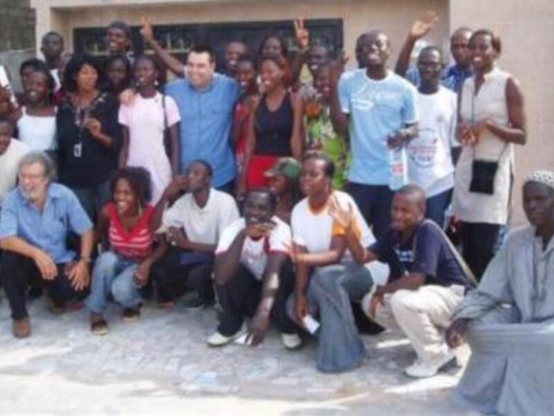 Grupo de personas reunidas en una escuela, sonrientes y felices, posando para una foto grupal.