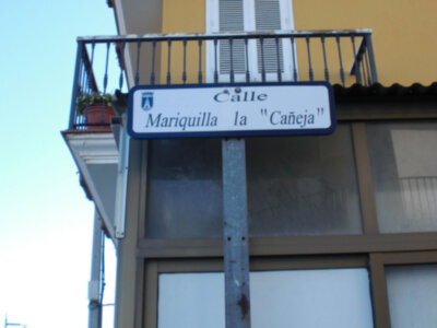 Placa indicativa de calle Mariquilla la Cañéja en un edificio con balcón y ventanas.