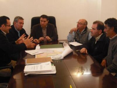 Gente en reunión, sillas, mesa con documentos y papeles.