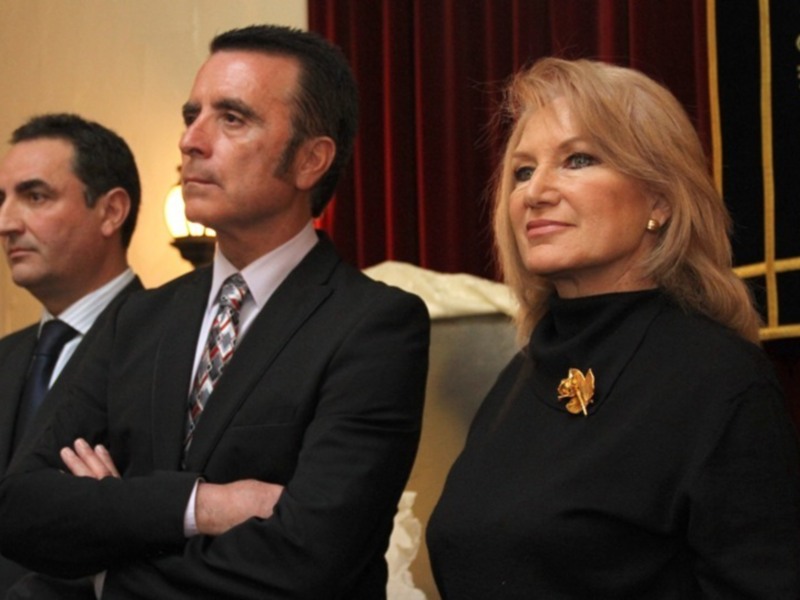 Tres personas en traje, dos hombres y una mujer con un broche dorado.