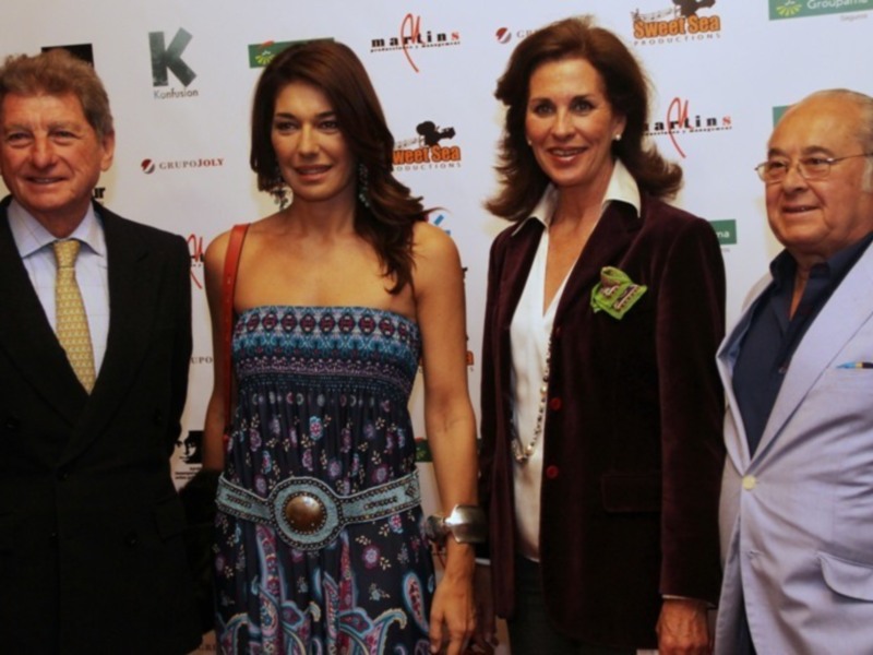 Fotografía de tres personas posando en un evento, con logos de empresas en el fondo.
