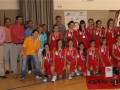 Equipo femenino de baloncesto posando con medallas y entrenadores en un gimnasio.