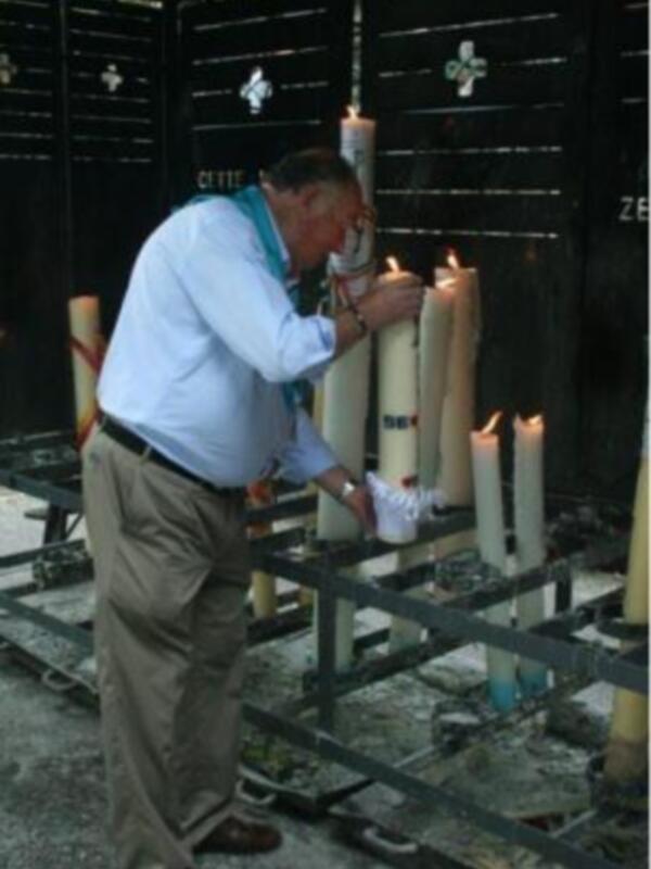Hombre encendiendo velas en un memorial con cruces talladas.