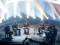 Un grupo de músicos en una escena de concierto, con luces brillantes y un fondo abstracto.