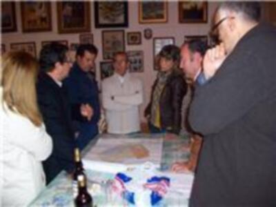 Un grupo de personas reunidas en una sala, con un hombre en el centro hablando mientras otros observan. La imagen muestra una reunión o conferencia, posiblemente en un contexto profesional o académico.