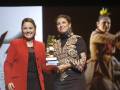 Dos mujeres sonrientes posan con un premio dorado en una ceremonia de premios.