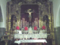 Altar con estatuas religiosas, velas encendidas y flores rojas.