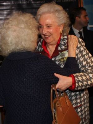 Dos personas abrazándose en un evento, con una mujer mayor sonriendo y otra con cabello blanco.