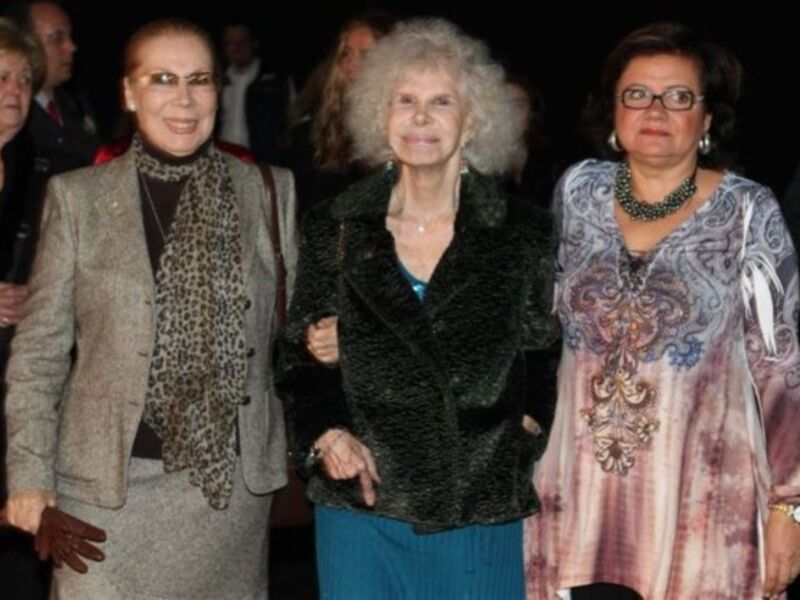 Tres mujeres mayores caminan juntas, dos de ellas con joyas y una con un abrigo estampado.