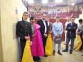 Grupo de personas en trajes formales, incluyendo un hombre con un sombrero de copa, posando en un entorno con estructuras metálicas y una iluminación de techo.